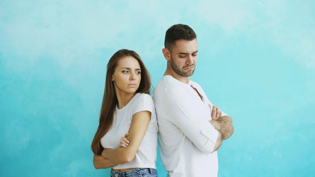 A woman and a man standing back to back with their arms crossed looking unhappy