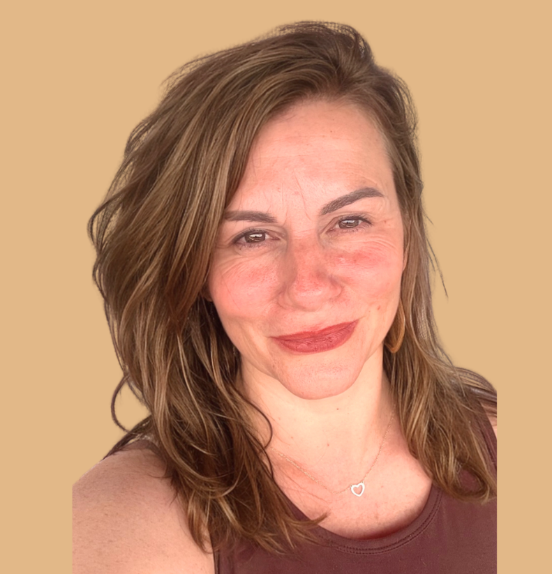 A woman with shoulder-length wavy brown hair, wearing a sleeveless top and a heart-shaped necklace, smiling against a beige background.