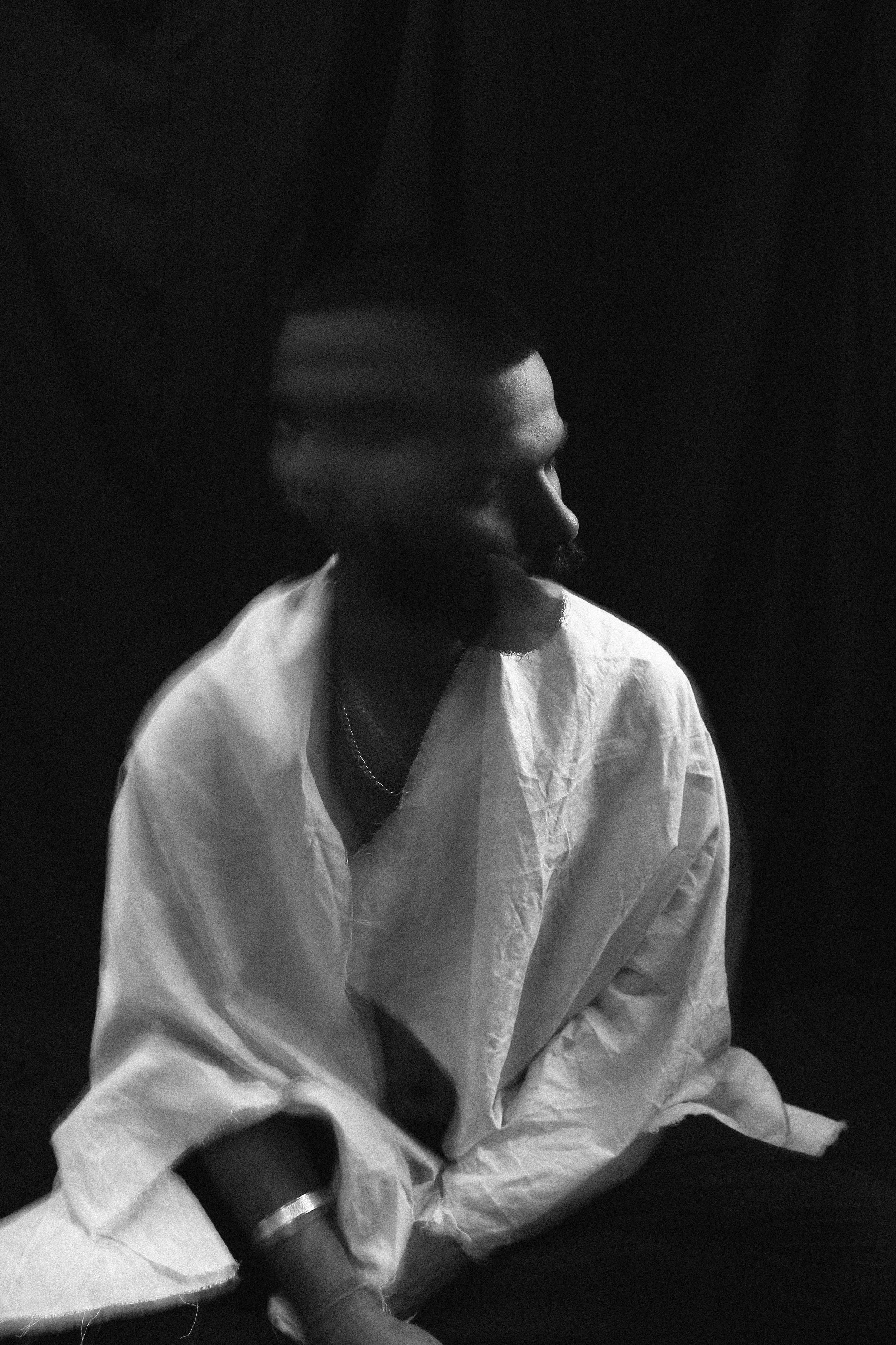 A black and white photo of a man sitting, wearing a white shirt, with his head turned to the side and looking away.