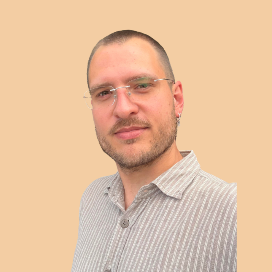 A young man with short hair, glasses, and a beard is wearing a collared shirt with beige and white stripes against a plain beige background.