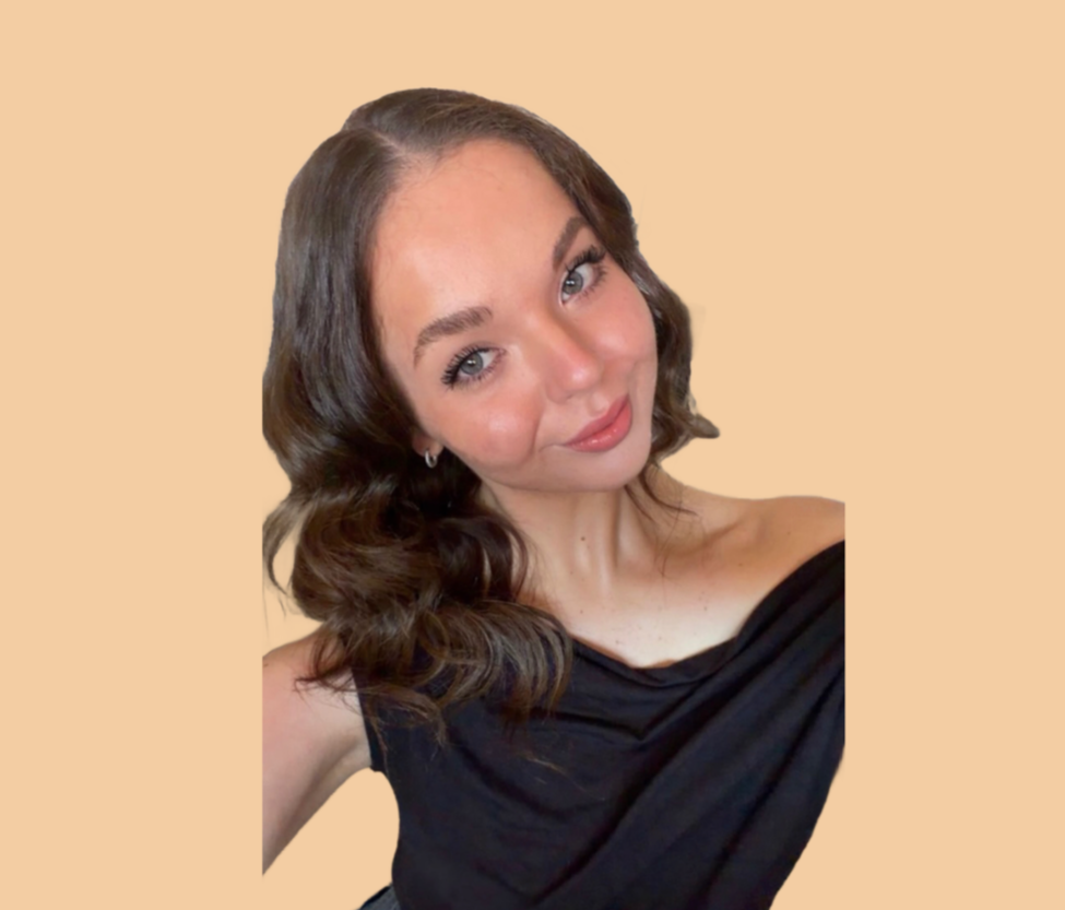 A woman with wavy brown hair and blue eyes, smiling slightly, wearing a black off-the-shoulder top, against a beige background.