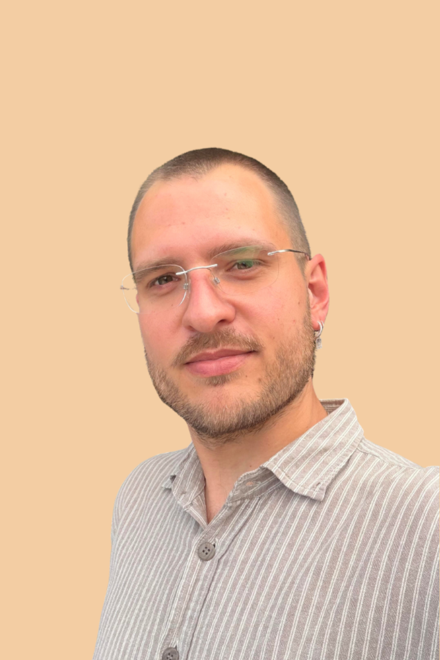 A man with short hair, wearing glasses, a light-colored striped shirt, and an earring, smiling slightly against a plain beige background.