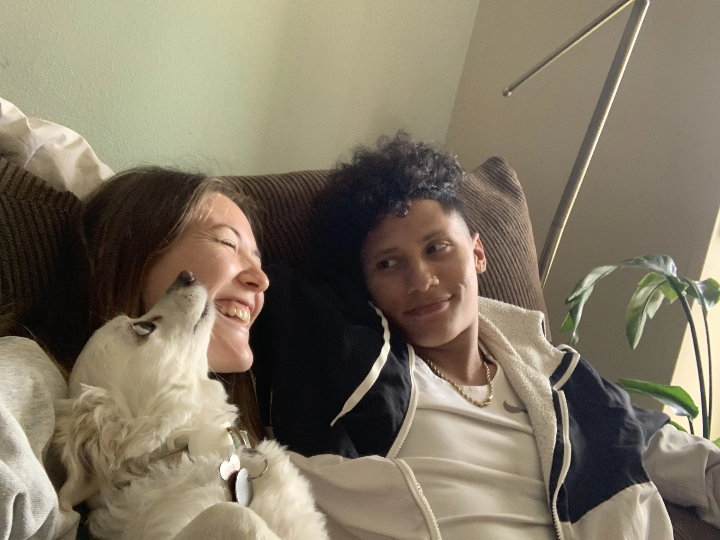 A woman, a young man, and a puppy lying on a sofa, smiling and looking at each other.