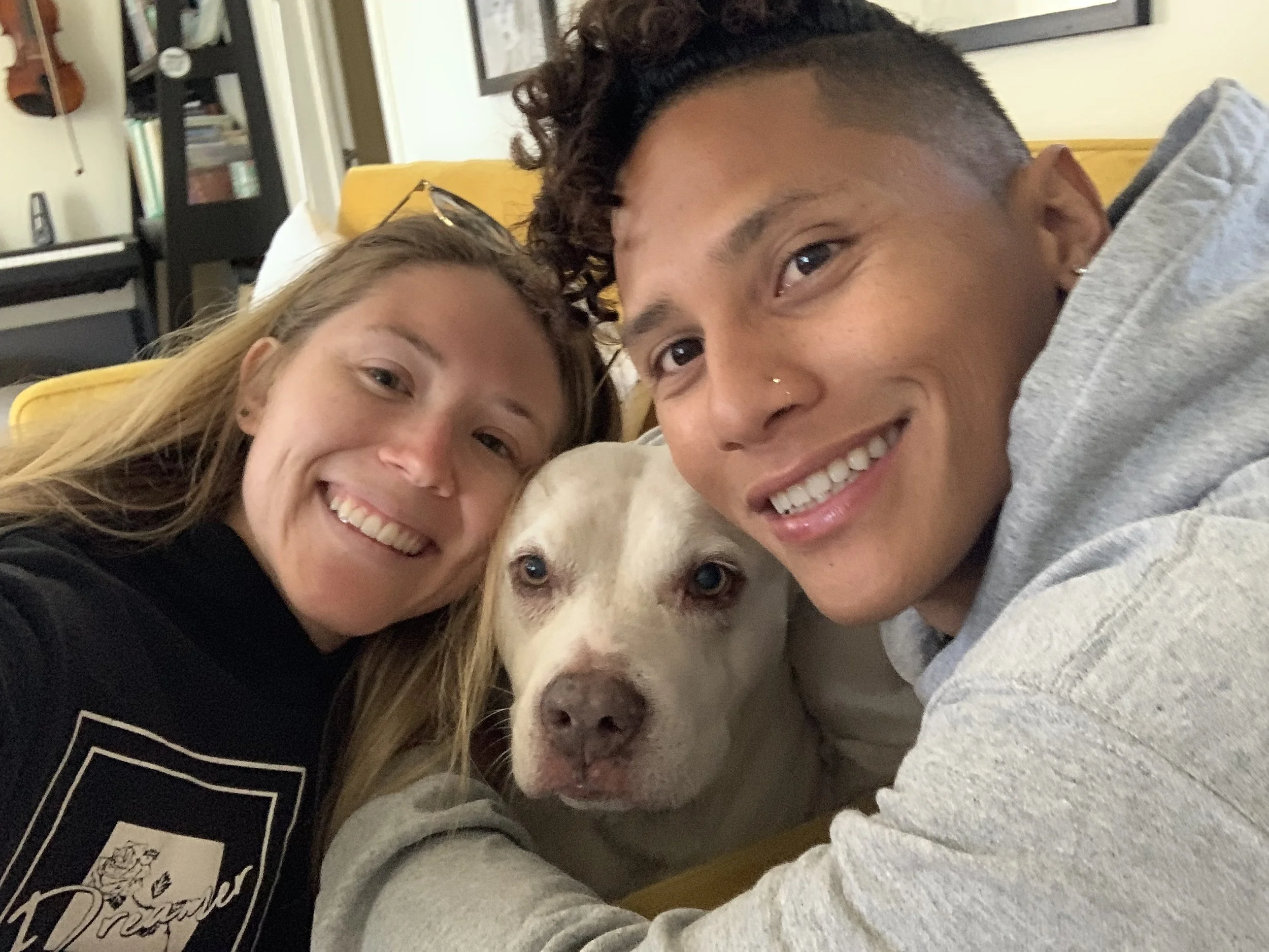 Two smiling women and a dog taking a selfie together in a cozy indoor setting.
