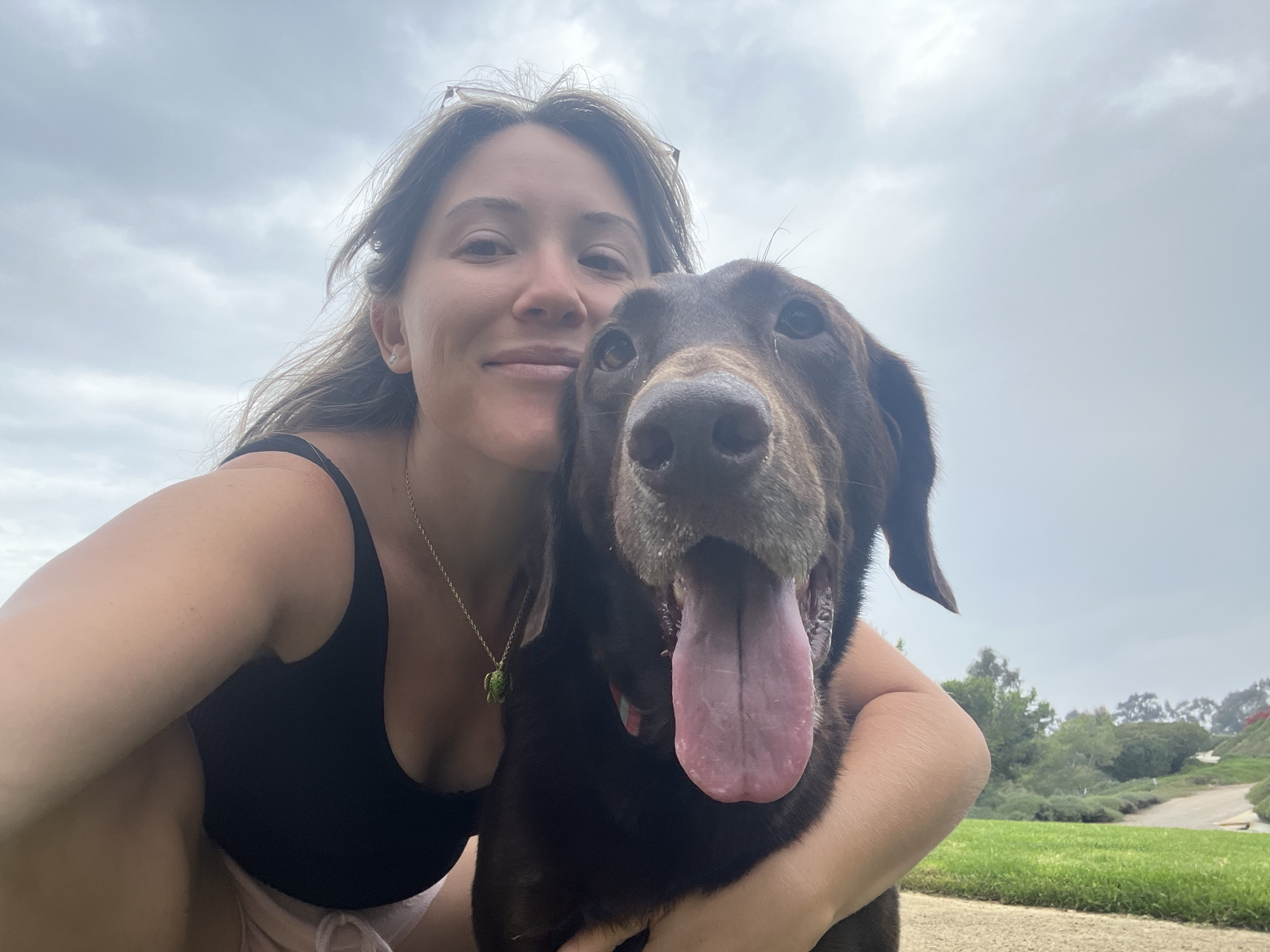 A woman and a large brown dog with a pink tongue hanging out, posing outdoors on a cloudy day.