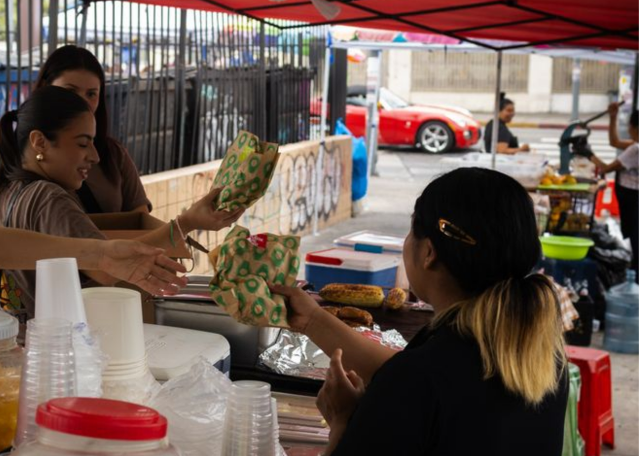Close-up of a smiling woman with curly hair, glasses, hoop earrings, and a striped blouse in a bright indoor setting.