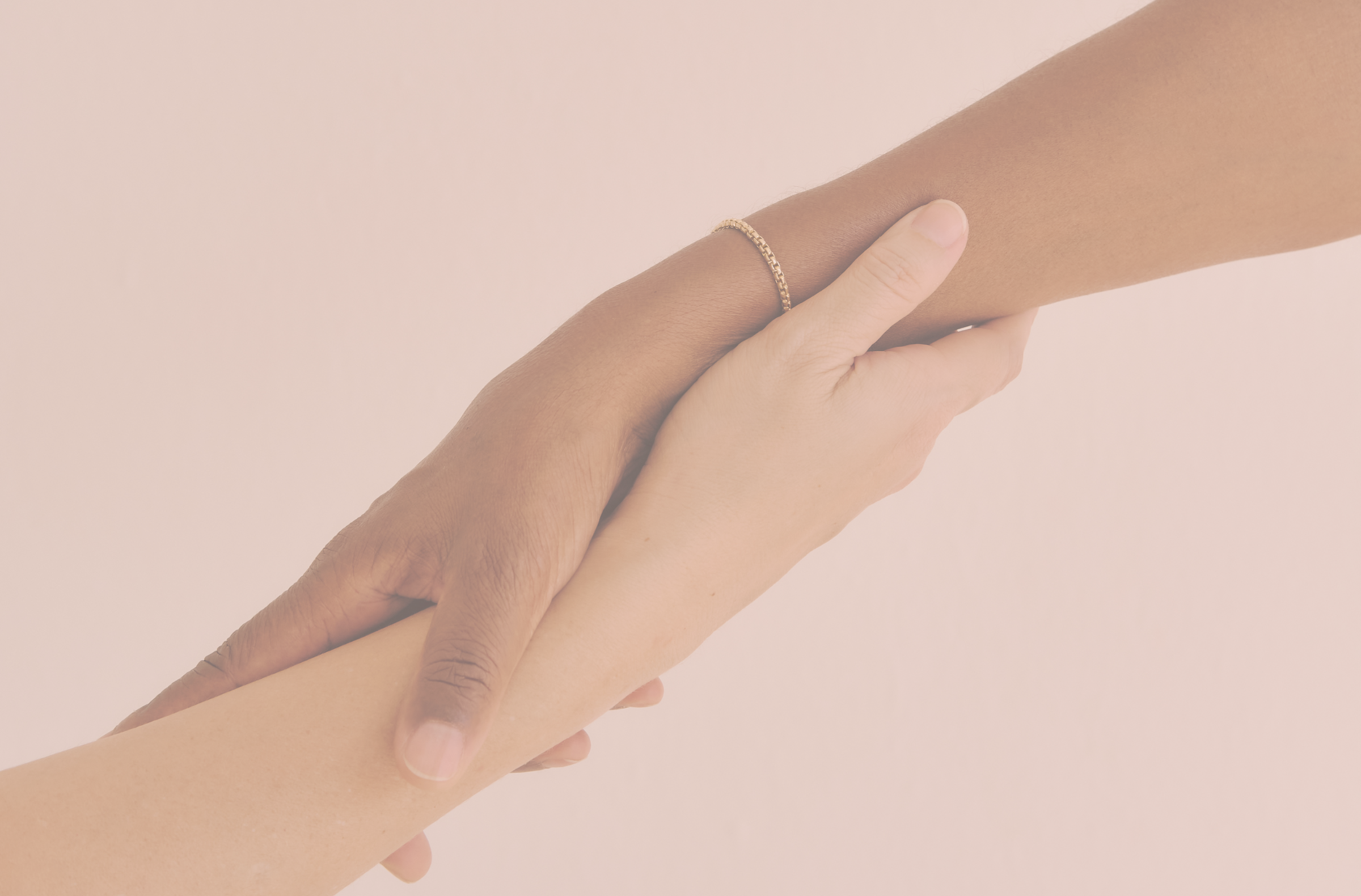 Two hands, one light-skinned and one dark-skinned, holding each other's wrists against a light pink background.
