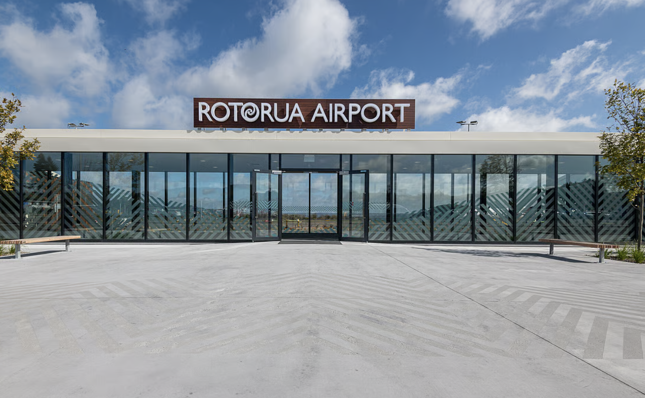 Front view of Rotorua Airport with glass doors and windows under a blue sky with clouds.