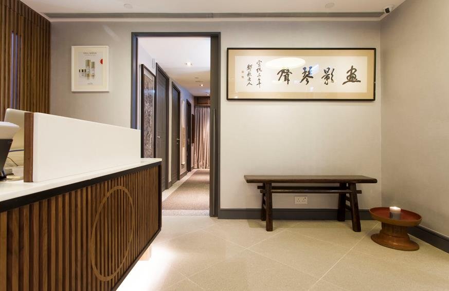 Bio Beauty Spa, a beauty boutique in Central Hong Kong by Wang Fang Construction, presents a serene, minimalist interior. A modern reception desk with a dark wood slatted base is complemented by framed abstract and calligraphy art. The neutral color 