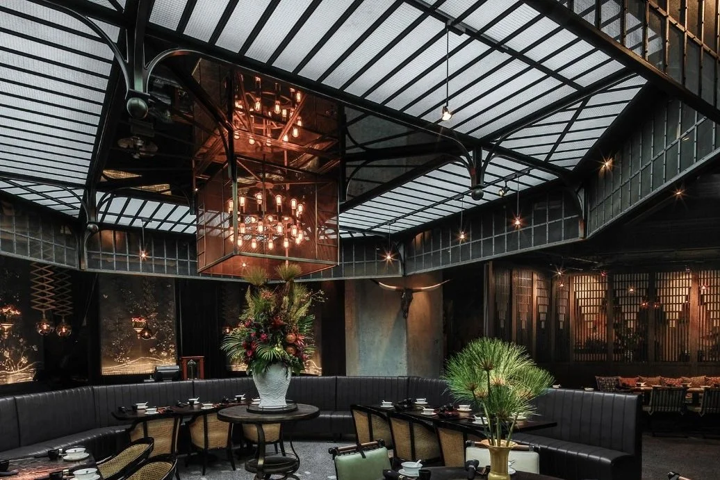 Mott 32, an award-winning Chinese Restaurant, interior dining area by Wang Fang Construction, featuring a large floral centerpiece, dark tables set for dining, and a mix of modern and rustic decor with a chandelier in the center, in Hong Kong Central