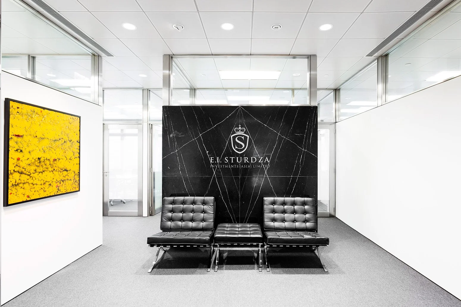 BBO office reception by Wan Fang Construction showing black marble wall panel with logo, vibrant yellow painting, black leather chair in Hong Kong Central.