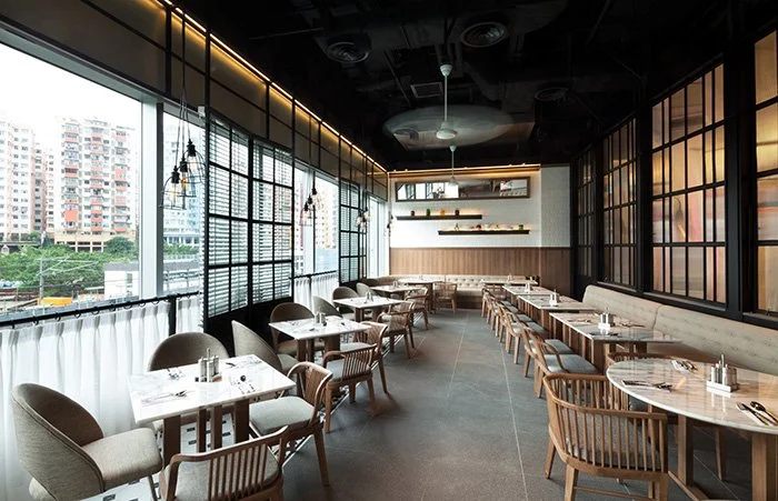 Made in HK, a modern restaurant in Hong Kong Kwun Tong by Wang Fang Construction, features an industrial-chic interior. Clusters of black pendant lights illuminate communal marble-topped tables. A geometric patterned tile floor and a wall of windows 