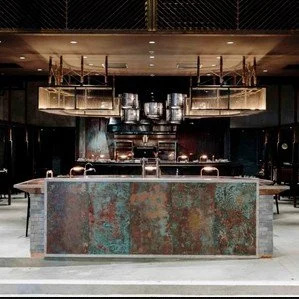 Rhoda modern restaurant with a central copper-toned bar counter by Wan Fang Construction, showing hanging pendant lights, shelving with bottles above, and a warm, dim lighting ambiance in Hong Kong, Sai Yin Pun.