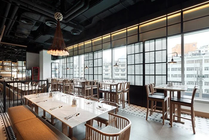 Made in HK, a modern restaurant in Hong Kong Kwun Tong by Wang Fang Construction, features an industrial-chic interior. Clusters of black pendant lights illuminate communal marble-topped tables. A geometric patterned tile floor and a wall of windows 