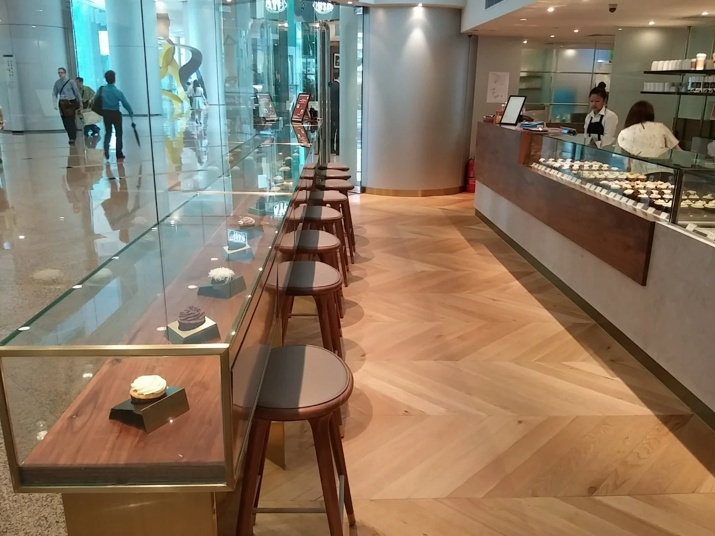 Sift, a modern patisserie in Quarry Bay Hong Kong by Wang Fang Construction, features a clean, inviting interior. A wooden counter with a glass display case showcases various pastries and desserts. The bright space has a herringbone-patterned wooden 