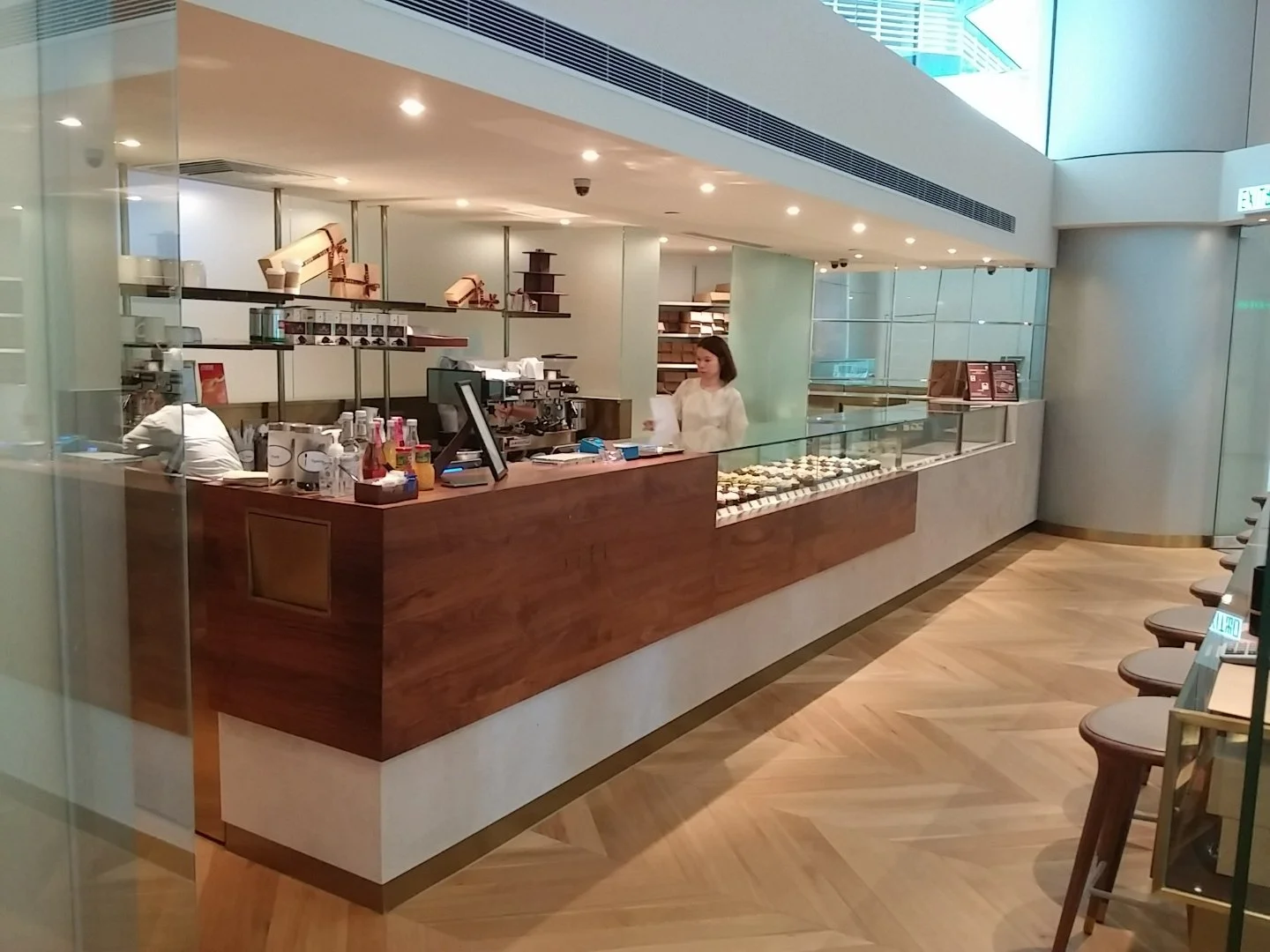 Sift, a modern patisserie in Quarry Bay Hong Kong by Wang Fang Construction, features a clean, inviting interior. A wooden counter with a glass display case showcases various pastries and desserts. The bright space has a herringbone-patterned wooden 