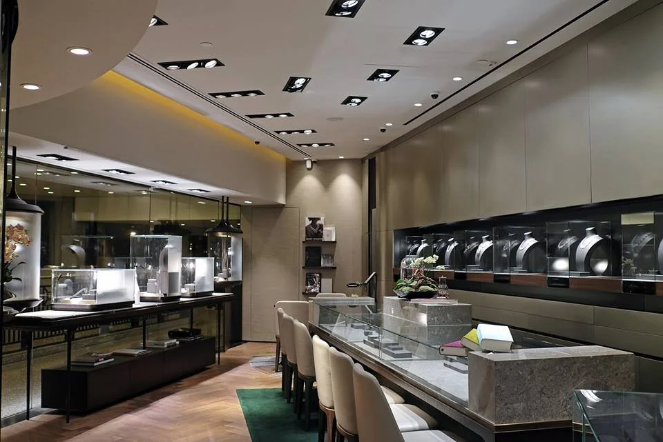 Carrera, a bespoke jeweller in The Galleria Central Hong Kong by Wang Fang Construction, features a luxurious interior. Elegant glass display cases, brightly illuminated, showcase necklaces and watches on grey platforms. The store's sophisticated atm