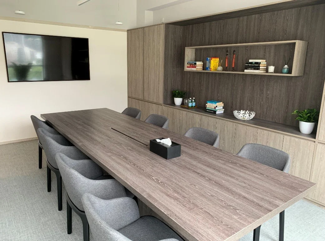 Partners Bay office workspace by Wan Fang Construction showing long wooden table, gray chairs, shelving unit with books and plant creating an organized atmosphere in Hong Kong Central.