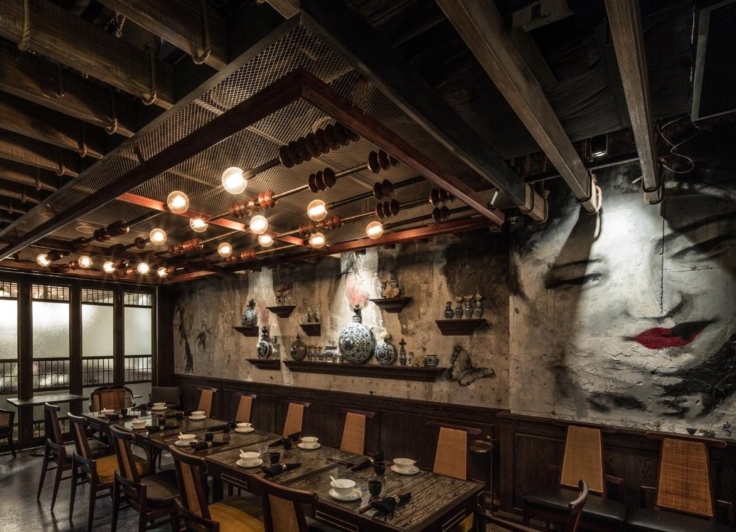 Mott 32, awarded Chinese Restaurant, interior dining area at a wall side by Wang Fang Construction, featuring a Chinese female with red lipstick drawing, dark tables set for dining, and a mix of modern and rustic decor with modern lighting works, in 
