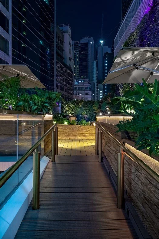 ICHU, an elegant restaurant and rooftop terrace by Wan Fang Construction. The foreground of the rooftop terrace features a wooden deck bordered by two metal handrails leading towards an area with green plants and seating under umbrellas. The deck has