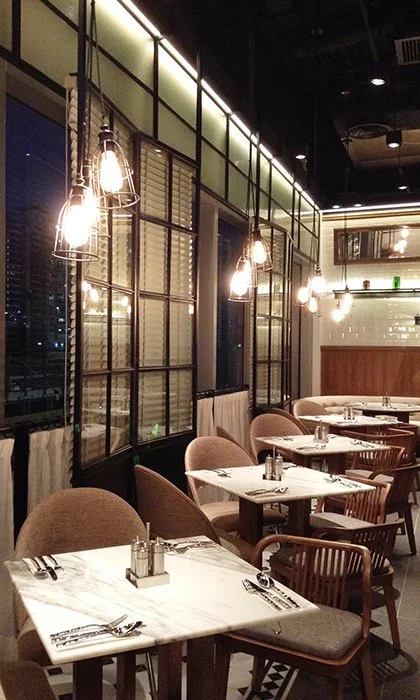 Made in HK, a modern restaurant in Hong Kong Kwun Tong by Wang Fang Construction, features an elegant interior with white marble-topped tables and pendant lights with cage designs. The neutral-toned chairs and warm wood accents create a contemporary,