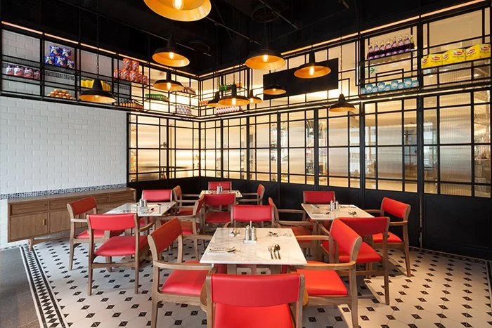 Made in HK, a modern restaurant in Hong Kong Kwun Tong by Wang Fang Construction features black pendant lights, red leather chairs, and white-topped tables. A long wooden counter and shelves of colorful utensils adorn the back wall, while a patterned