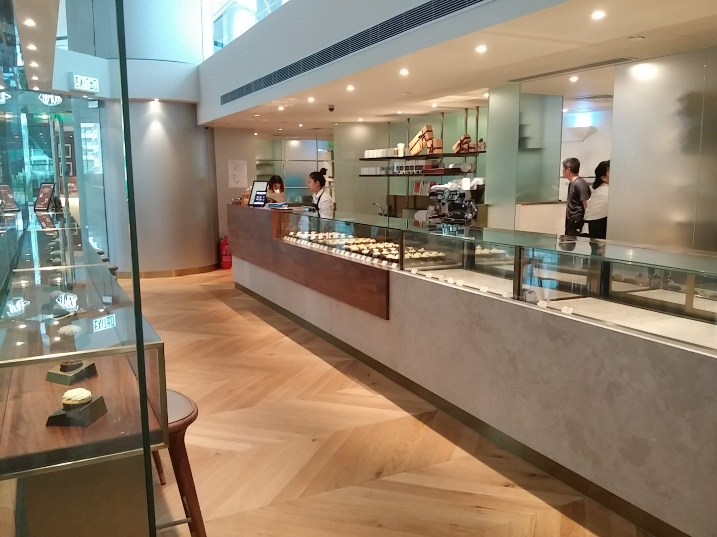 Sift, a modern patisserie in Quarry Bay Hong Kong by Wang Fang Construction, features a clean, inviting interior. A wooden counter with a glass display case showcases various pastries and desserts. The bright space has a herringbone-patterned wooden 