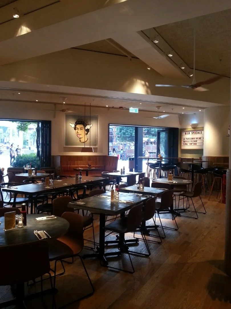 Beef & Liberty, a gourmet burger restaurant in Stanley Hong Kong by Wang Fang Construction, features a modern interior. The space has an exposed ceiling with recessed lighting and fans over polished hardwood floors. Long communal tables with leather 