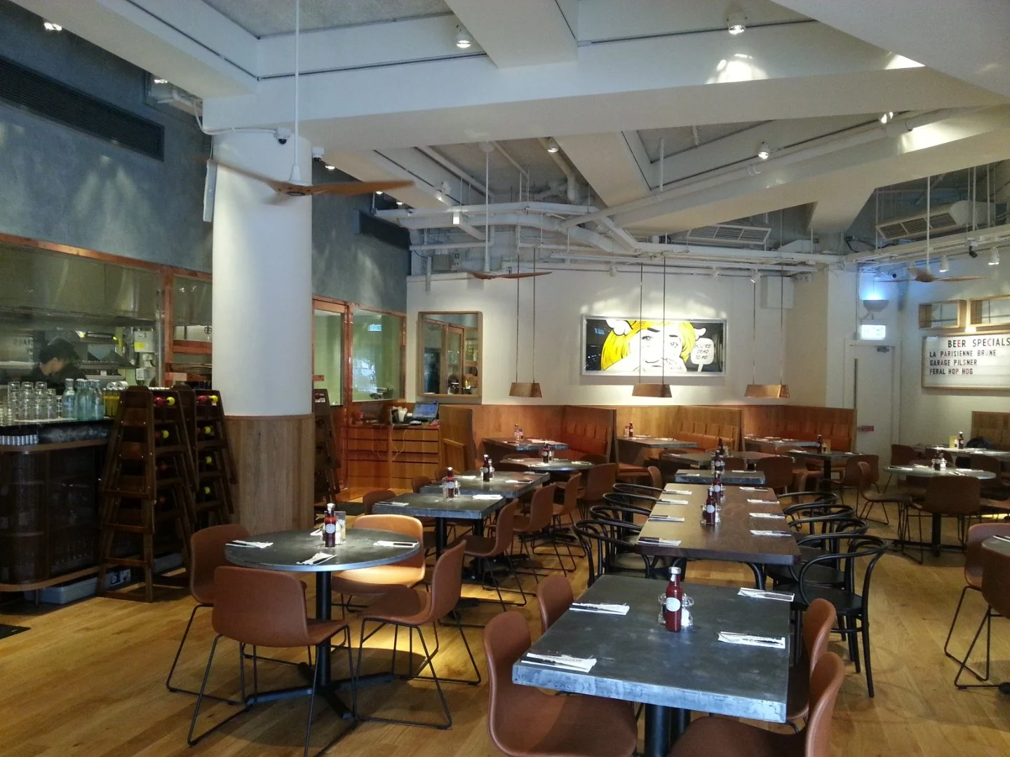 Beef & Liberty, a gourmet burger restaurant in Stanley Hong Kong by Wang Fang Construction, features a modern interior. The space has an exposed ceiling with recessed lighting and fans over polished hardwood floors. Long communal tables with leather 