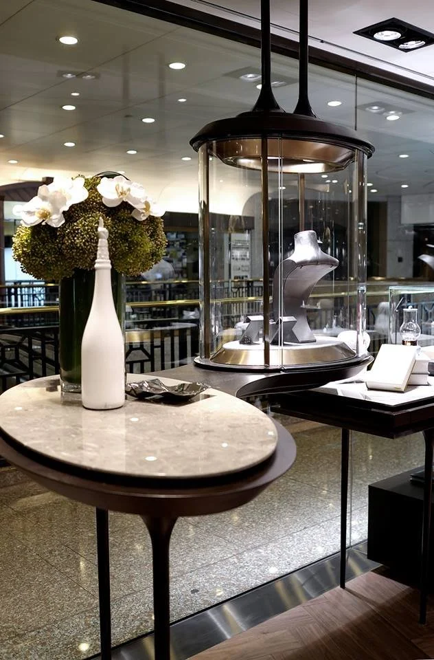 Carrera, a bespoke jeweller in The Galleria Central Hong Kong by Wang Fang Construction, features a luxurious interior. Elegant glass display cases, brightly illuminated, showcase necklaces and watches on grey platforms. The store's sophisticated atm