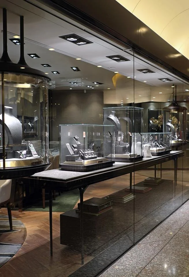 Carrera, a bespoke jeweller in The Galleria Central Hong Kong by Wang Fang Construction, features a luxurious interior. Elegant glass display cases, brightly illuminated, showcase necklaces and watches on grey platforms. The store's sophisticated atm