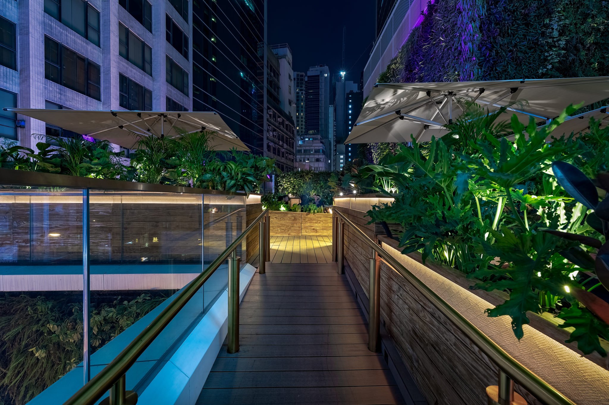 ICHU, an elegant restaurant and rooftop terrace by Wan Fang Construction. The foreground of the rooftop terrace features a wooden deck bordered by two metal handrails leading towards an area with green plants and seating under umbrellas. The deck has