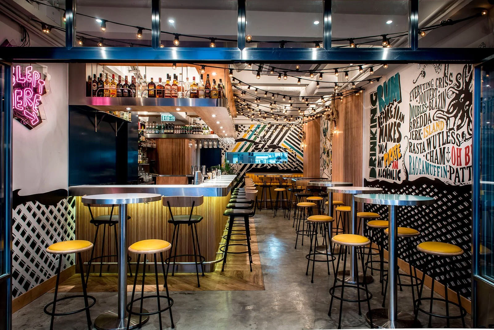 Rummin' Ting, a Caribbean-inspired bar and restaurant in Central Hong Kong by Wan Fang Construction, features a vibrant interior. A central, backlit bar displays bottles, surrounded by stools and round tables with distinctive yellow seats. The modern