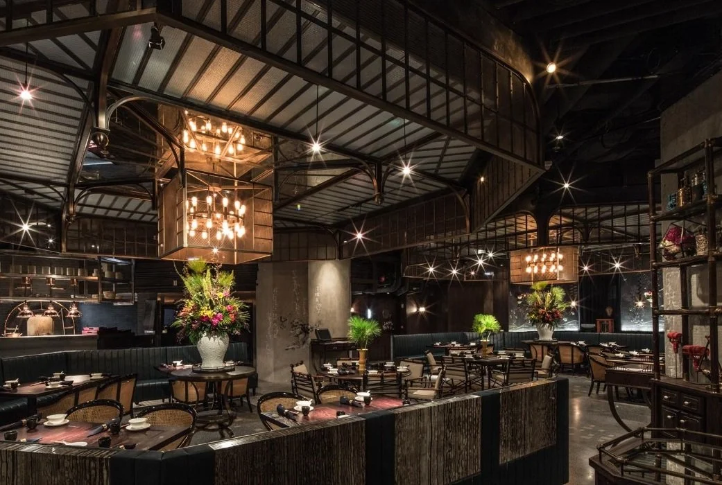 Mott 32, an award-winning Chinese Restaurant, interior dining area by Wang Fang Construction, featuring a large floral centerpiece, dark tables set for dining, and a mix of modern and rustic decor with a chandelier in the center, in Hong Kong 