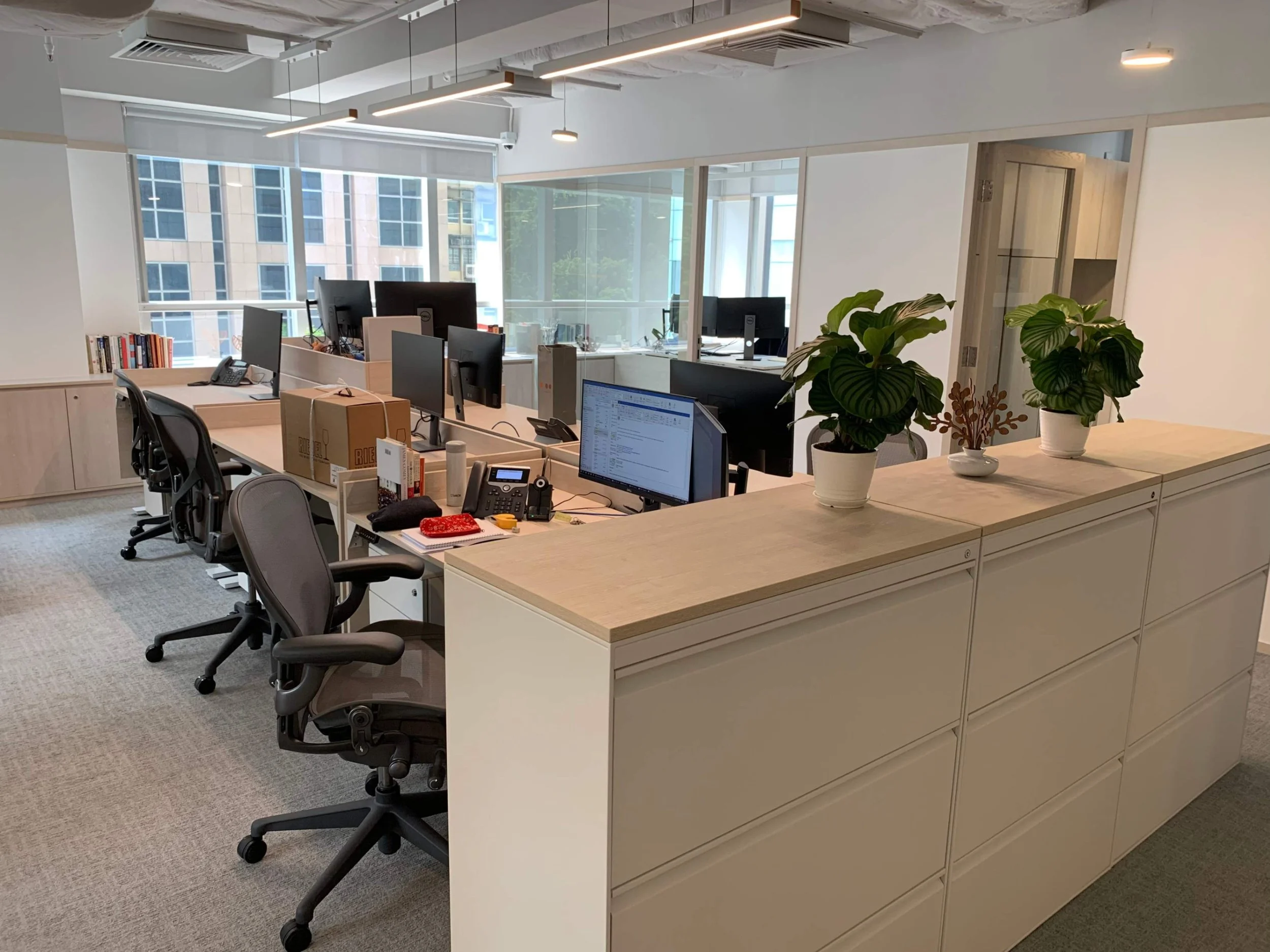 Partners Bay office workspace by Wan Fang Construction showing wooden desk, gray chairs, shelving unit with plants creating an organized atmosphere in Hong Kong Central.