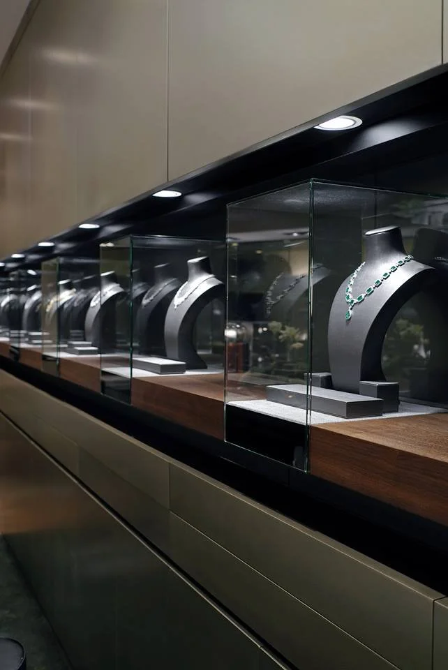 Carrera, a bespoke jeweller in The Galleria Central Hong Kong by Wang Fang Construction, features a luxurious interior. Elegant glass display cases, brightly illuminated, showcase necklaces and watches on grey platforms. 