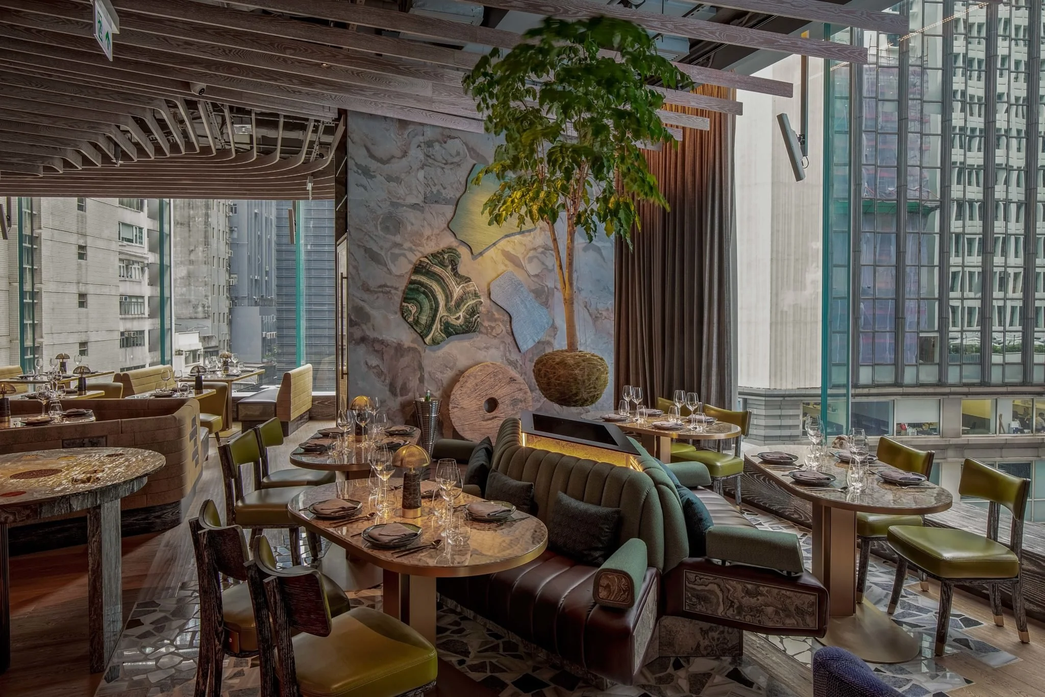 ICHU, elegant restaurant interior by Wan Fang Construction, showing round marble tables, green chairs, and a high-backed green booth in Hong Kong Central.