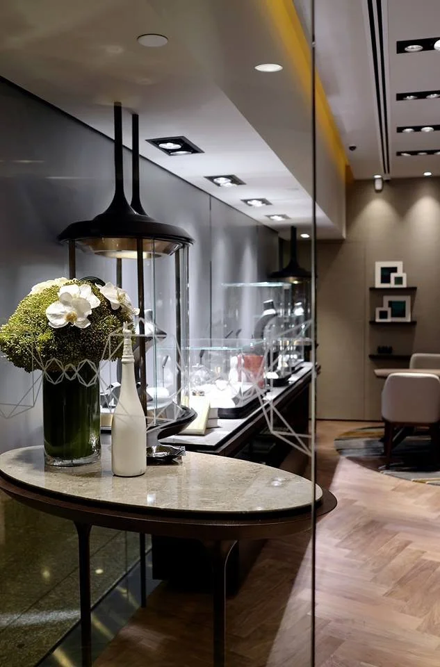 Carrera, a bespoke jeweller in The Galleria Central Hong Kong by Wang Fang Construction, features a luxurious interior. Elegant glass display cases, brightly illuminated, showcase necklaces and watches on grey platforms. The store's sophisticated atm