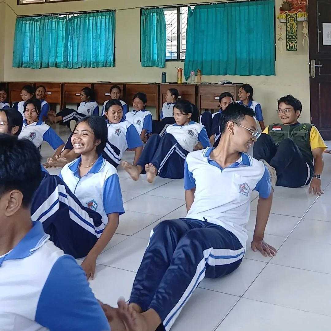 School students in uniforms sitting on the classroom floor, smiling and laughing.
