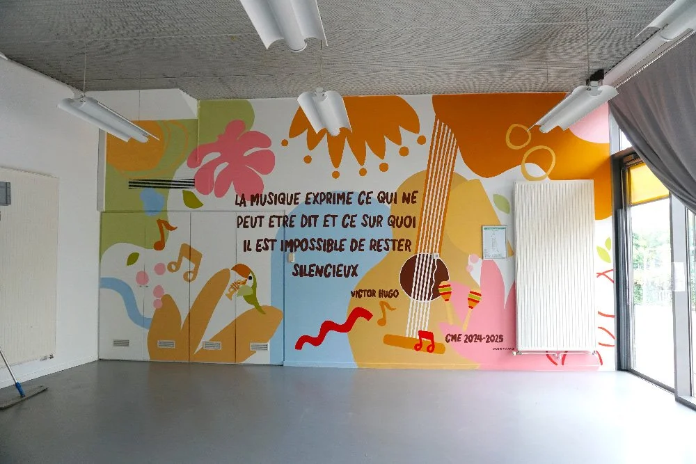 Fresque murale colorée dans une école de musique, une guitare et un oiseau, avec une citation en français de Victor Hugo sur la musique, dans une salle avec fenêtres et rideaux.