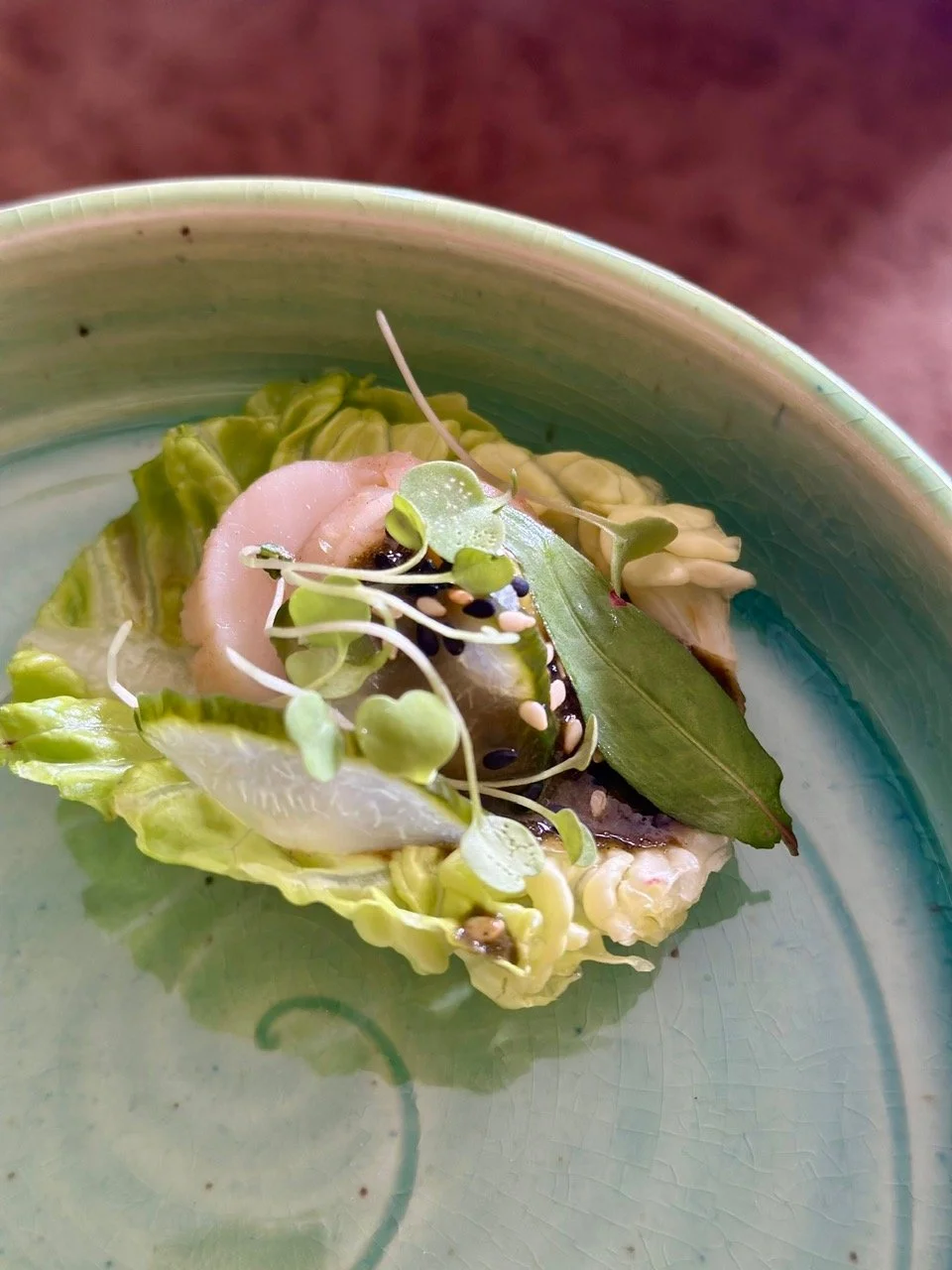 Close-up of a small salad with lettuce, microgreens, lemon, and herbs served on a green ceramic plate.