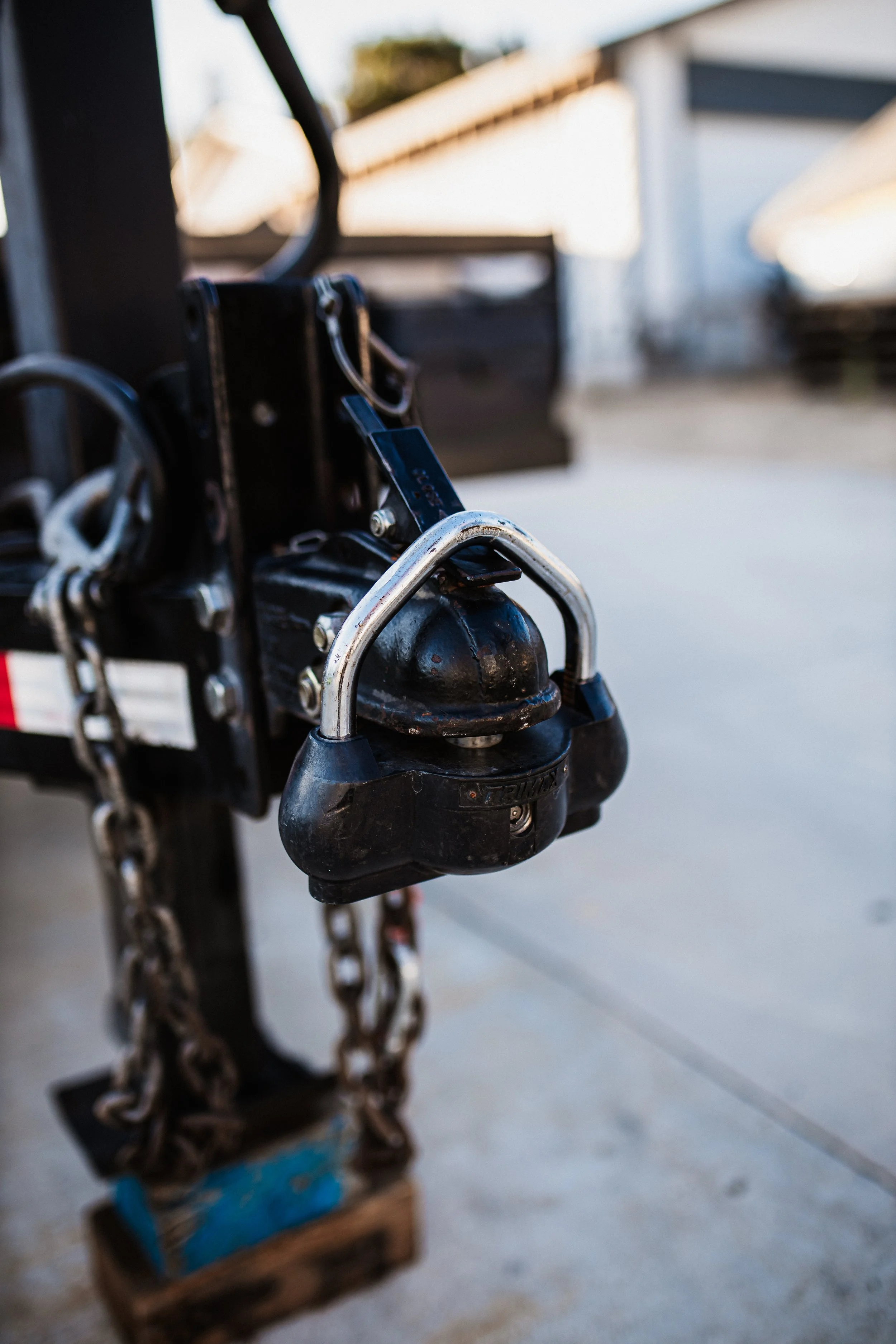 Close-up of a trailer hitch coupler with chains, mounted on a trailer in an outdoor setting.
