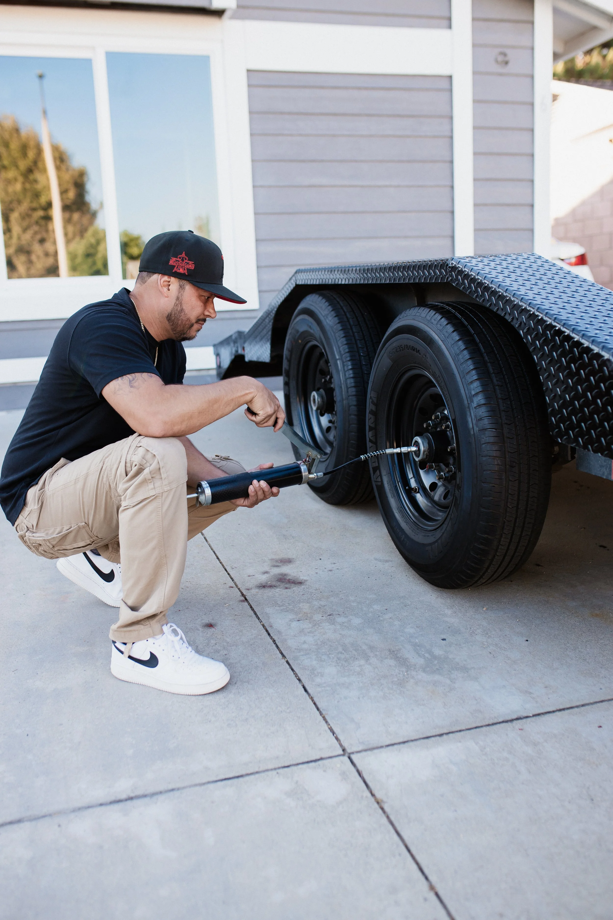 A man is crouched down and inflating a tire on a flatbed trailer using a portable air compressor.