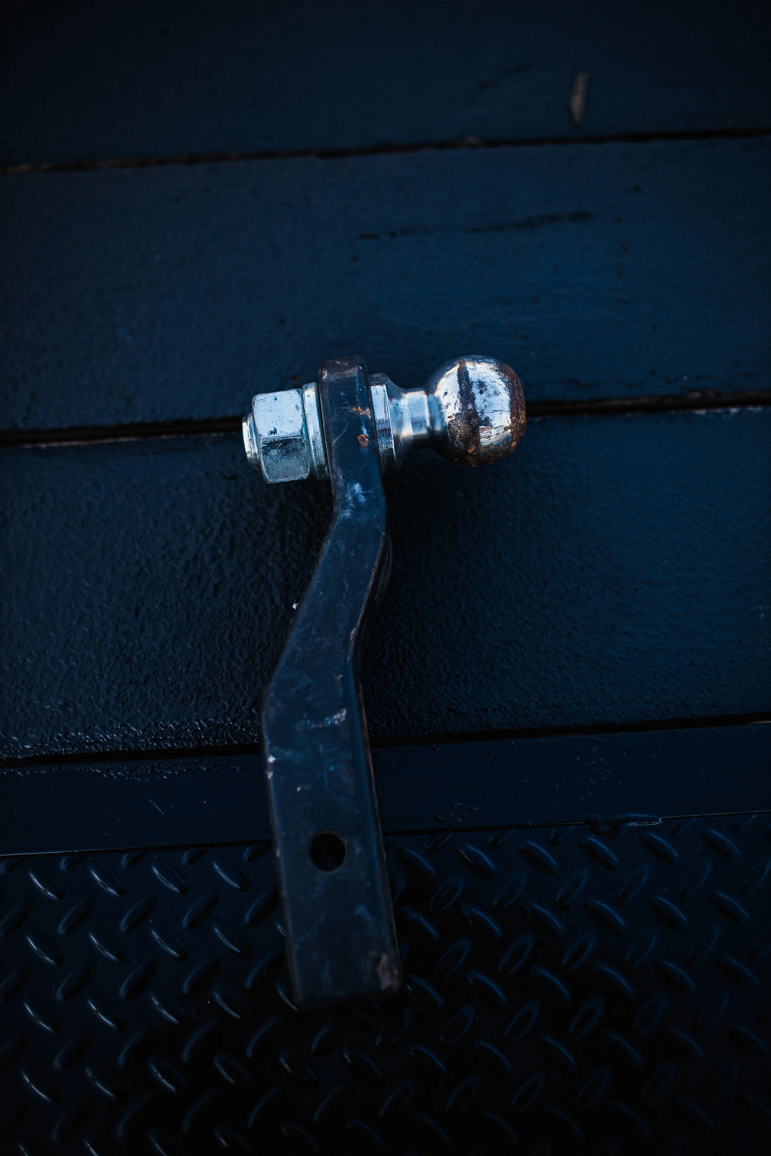 Close-up of a hitch ball with a metal arm on a black textured surface.