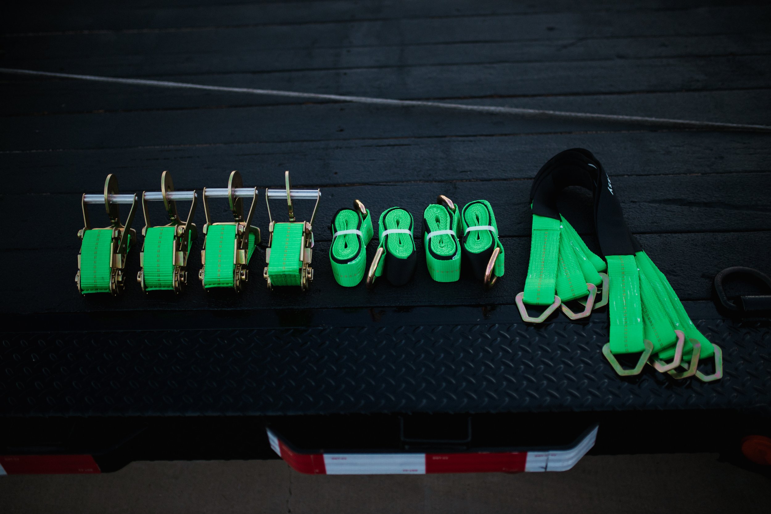 Various green and black lifting straps, secured with metal clasps, arranged on a black surface, likely for weightlifting or strength training.