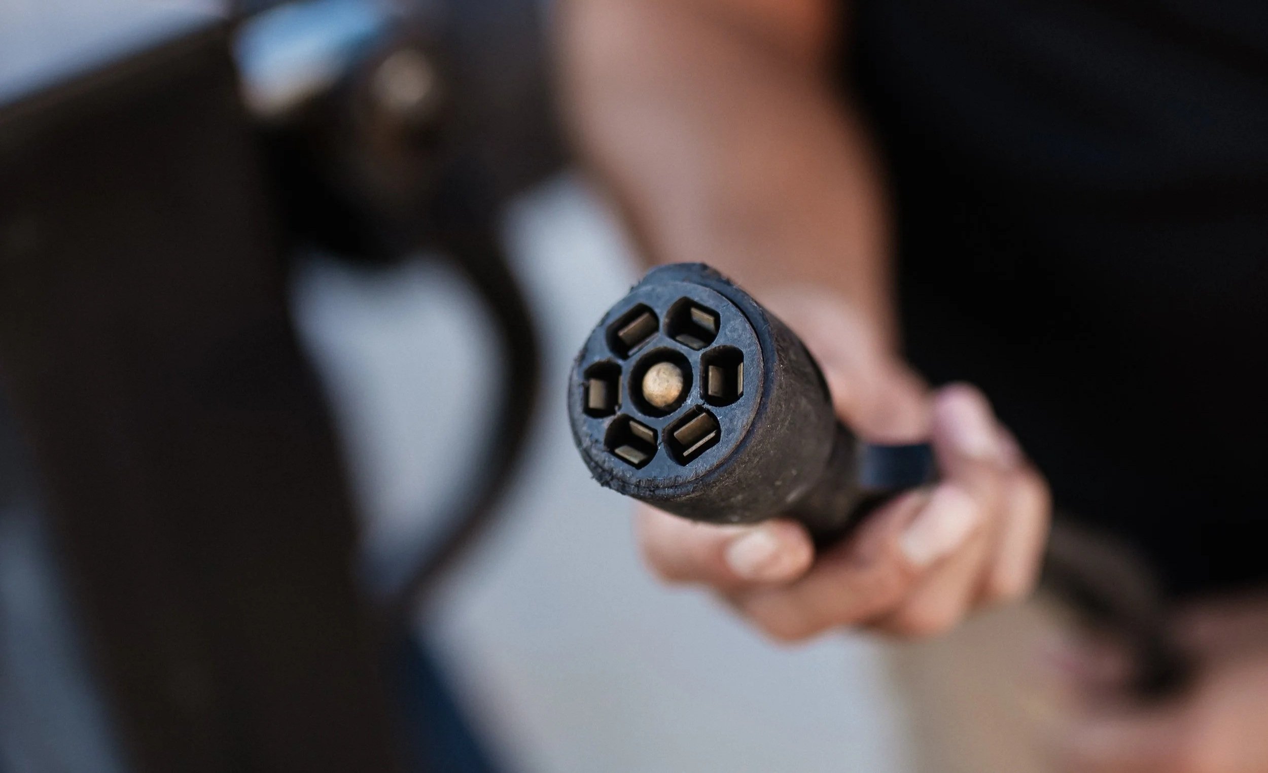 Close-up of a person's hand holding a black handgun, showing the barrel's muzzle with multiple holes.