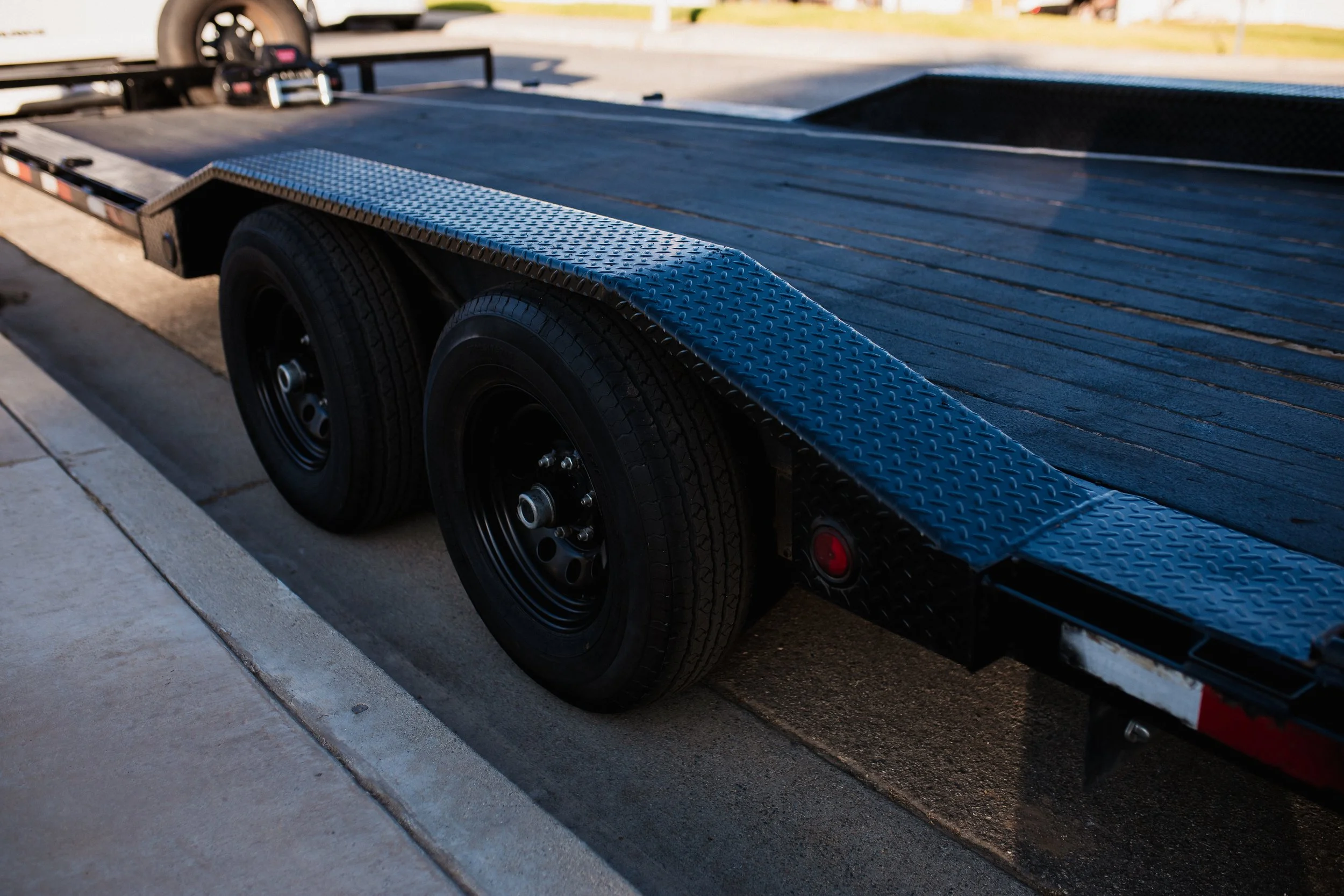 Close-up of a black flatbed trailer with two wheels parked on a paved street.
