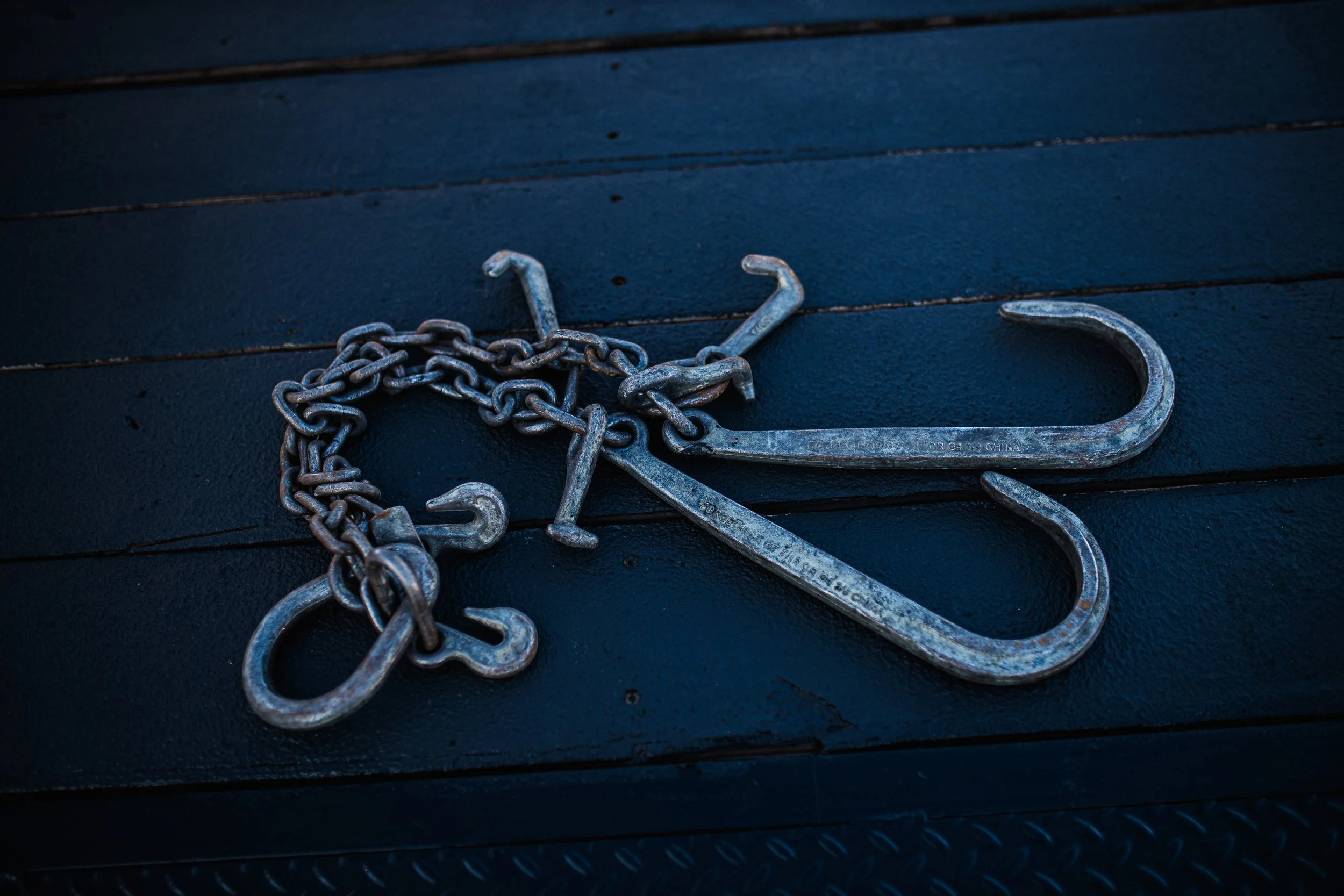 A pair of metal hooks and a chain lying on a black textured surface.