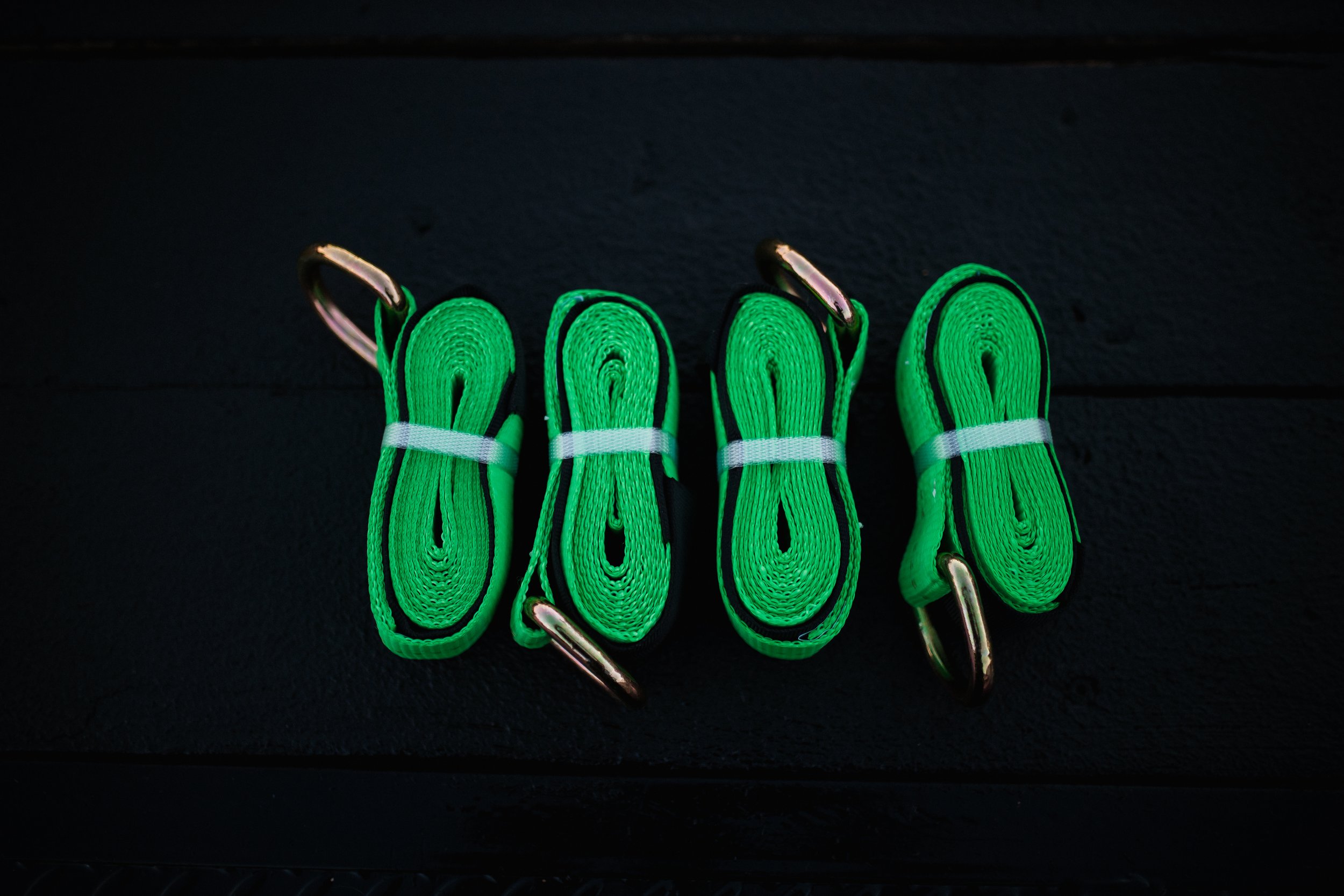 Four neon green straps with metal hooks at each end, arranged parallel on a black surface.