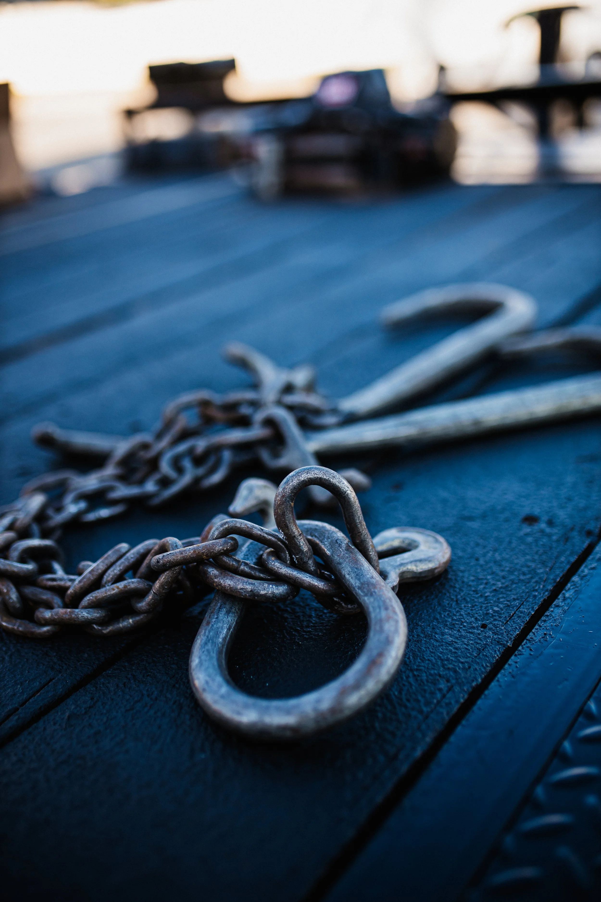 Close-up of a rusty metal chain and anchor on a black surface, blurred background with outdoor setting.